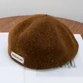Detailed close-up of brown wool newsboy cap with brand label on a magazine - Adjustable / Caramel