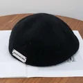 Detailed texture of black wool beret with a white minimalist woven letter label - Adjustable / Black