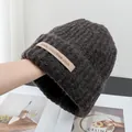Detail view of thick knit texture and leather label on dark brown wool blend beanie - Stretchy / Coffee