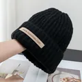 Close-up of black ribbed knit beanie with brown brand label on white background - Stretchy / Black