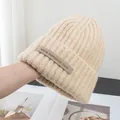 Detail of beige knit beanie showing ribbed texture and woven label in a lifestyle setting - Stretchy / Apricot