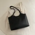 Bolso tote de cuero sintético negro con logo dorado sobre blazer crema y libro de arte - Negro