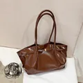 Dunkelbraune glänzende Shopper-Tasche mit goldener Schnalle in weichem Licht - Braun
