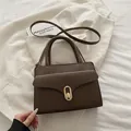 Dunkelbraune Handtasche mit Litschi-Muster, goldenem Schloss und Riemen auf weißem Stoff - Braun