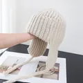 Detailed close-up of beige chunky ribbed knit trapper hat with braided earflaps ties - M (56-58cm) / Off White