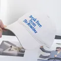 Detail of embroidered 'Break Free From The Routine' text on a cream baseball cap - Adjustable / Off White