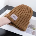 Detail of brown ribbed knit beanie featuring a purple brand patch on wood background - Stretchy / Camel