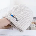 Detailed close-up of cream knit beanie featuring dachshund embroidery and ribbed texture - Beige