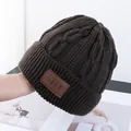Detailopname van de dikke kabelgebreide textuur en het bruine leren label op de wintermuts - Eén Maat(Elastisch) / koffiekleur