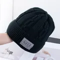 Detailopname van zwarte dikke gebreide muts met leren label en winterse textuur - Eén Maat(Elastisch) / Zwart