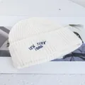 Detail view of cream knit beanie featuring navy New York 1986 embroidery on ribbed cuff - Stretchy / White