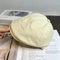 Détail du tissu de la casquette beige avec bouton décoratif posée sur un livre - Réglable / Poche zippée