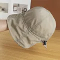 Detail of beige bucket hat with cross stitching and adjustable drawstring on wood surface - Adjustable / Khaki