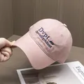 Détail de casquette rose en coton avec broderie bleue sur un fond en bois naturel - Réglable / Rose