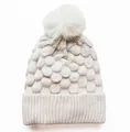 Nahaufnahme des groben Strickmusters und weißen Kunstfellbommel an der Strickmütze - Beige
