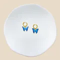 Detail von goldenen Creolen mit blauen Schmetterlingsanhängern auf Keramik-Display - Blauer Schmetterling Stil (#20)