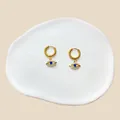 Detailansicht der goldenen Evil Eye Ohrringe mit blauen Steinen auf weißer Keramikschale - Blaues Evil Eye Anhänger Stil (#35)