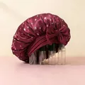 Close-up of burgundy satin hair bonnet with cherry print and large decorative bow - Burgundy