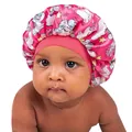 Pink satin baby sleep bonnet with unicorn print and elastic band on infant model - Rose Red
