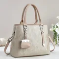 Detail of cream luxury handbag showing metallic texture and creative mini bag charm - Apricot