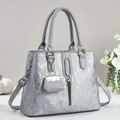 Detailopname van zilveren tote tas met metalen kwastje en mini tasvormige accessoire - Grijs