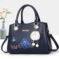 Deep blue embroidered handbag with golden hardware and white plush charm on a clean background - Blue