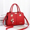 Elegant red PU leather handbag with gold hardware and pearl floral pendant on a desk - Red