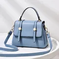 Detail of light blue square crossbody bag with gold hardware and top handle on table - Blue