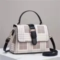 Retro plaid crossbody bag with black leather trim and gold hardware on marble stand - Khaki