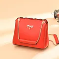 Red leather crossbody bag featuring a metal bow, rhinestone drop, and gold chain strap - Red