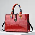 Detailed macro view of red crocodile-embossed handbag with silk scarf on handle and gold lock - Red