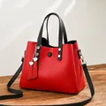 Fashionable red PU leather handbag with black straps and heart charm on wooden surface - Red