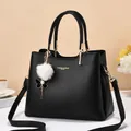 Sac à main en cuir noir avec détails dorés et pompon en peluche sur un bureau chic - Noir