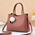 Close-up of pink leather handbag featuring gold hardware and a fluffy pom-pom charm - Pink