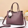 Detailed view of mauve lychee leather handbag featuring gold hardware and a fur charm - Purple