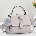 Detail of light beige lychee pattern leather handbag featuring golden oval lock and fur ball - Gray