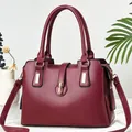 Dettaglio macro della borsa rosso vino con hardware dorato e profilo a trapezio elegante - Rosso