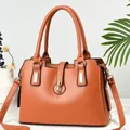 Macro shot of caramel leather handbag featuring gold metal ring lock and dual handles - Earthy Yellow