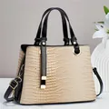 Detailaufnahme der beigen Handtasche mit Krokodilprägung, schwarzen Kanten und Goldbeschlägen - Khaki