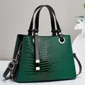 Detail view of dark green crocodile embossed handbag with sleek black handles and gold hardware - Green