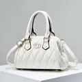 Detalle de bolso acolchado blanco con hebilla de corazón dorado en base minimalista - Blanco Roto
