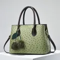 Detail of ostrich-textured green tote bag with cherry pompom charm and gold hardware - Green