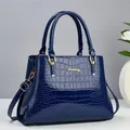 Detailopname van donkerblauwe handtas met krokodillenreliëf en goudkleurig metalen logo - Blauw