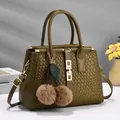 Close-up of olive green woven leather bag with gold buckle and cherry fur ball charms - Green