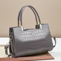 Detail of grey crocodile embossed glossy handbag with golden hardware and brand logo - Gray