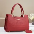 Detail of red crocodile pattern handbag with gold logo, metal feet, and strap - Red