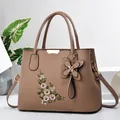 Détail d'un sac à main marron avec broderie florale élégante et pendentif papillon doré - Kaki