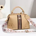 Détail du sac docteur kaki avec rayures rouge-vert, nœud doré et bandoulière brodée - Or