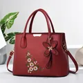 Detailed close-up of dark red handbag with floral embroidery and butterfly pendant - Wine Red