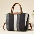 Detail of striped canvas tote showing brown leather handles and golden metal hardware - Black